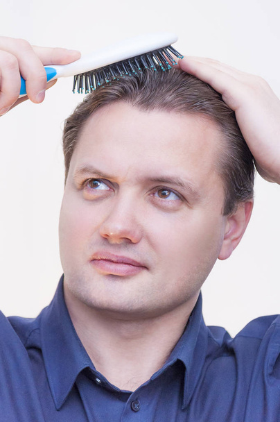 Portrait of young Caucasian Ethnicity man with blue shirt brushing combing hair with hairbrush on white background - Photo, Image