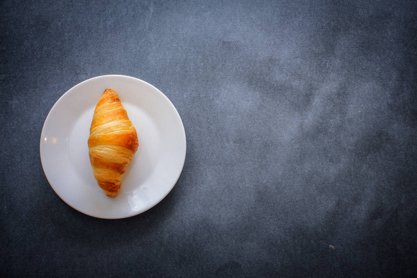 A rich variety of food photography Croissant.One delicious croissant on a dessert white plate on dark craft paper. - Foto, immagini
