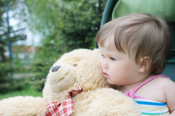baby girl portrait sitting in baby carriage with teddy bear toy together at summer looking away - 写真・画像