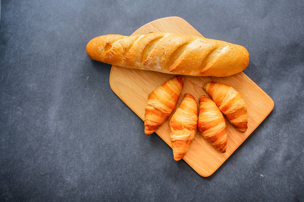 French loaf and four croissants on a wooden cutting board on dark craft paper. - Fotoğraf, Görsel
