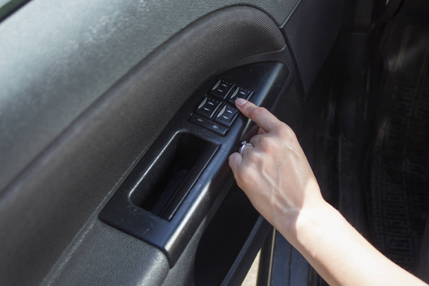 A woman's hand touches the window adjustment button in the car. - Фото, зображення