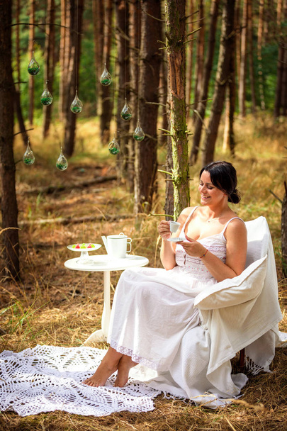 Vrouw is het drinken van koffie in de ochtend op de achtergrond van de natuur van bos - Foto, afbeelding