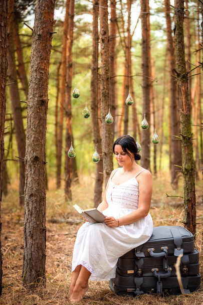 Kobieta czyta książki na walizki rano na tle przyrody lasu - Zdjęcie, obraz