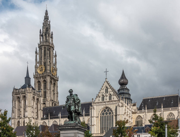 Antwerpen, België - 24 September 2018: Peter Paul Rubens bronzen standbeeld met torens, schip en koor van Onze-Lieve-Vrouwe Kathedraal van onze lieve vrouw in terug onder witte bewolkte hemel. - Foto, afbeelding