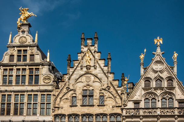 Antverpy, Belgie - 24 září 2018: Zlaté sochy na vrcholu fasády cechovní domy na náměstí Grote Markt. Hnědé kameny, oblouky pod modrou oblohou. - Fotografie, Obrázek