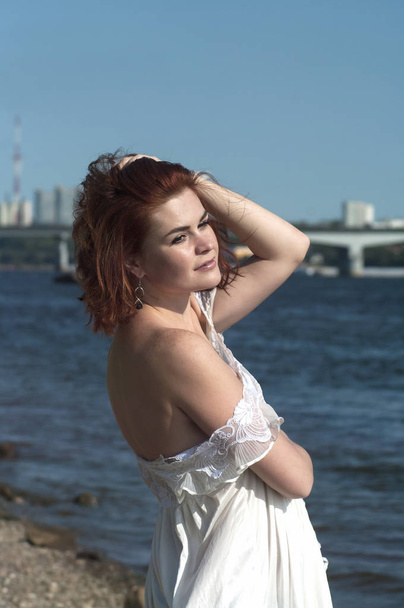 Young girl in light dress on the background of the river and the city.Emotionally posing. - Фото, изображение