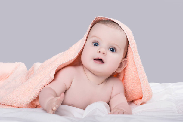 Baby with big blue eyes lying on belly under the pink towel after shower, isolated over gray background - Fotó, kép