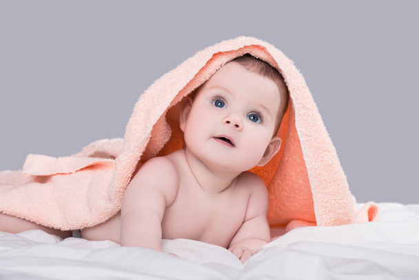 Baby with big blue eyes lying on belly under the pink towel after shower, isolated over gray background - Foto, afbeelding