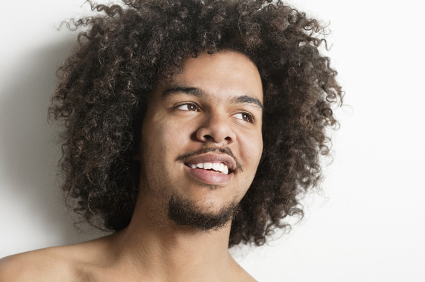 Nahaufnahme eines glücklichen jungen Mannes mit lockigem Haar, der vor weißem Hintergrund wegschaut - Foto, Bild