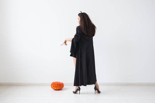 Mujer morena sonriente en Halloween maquillaje posando con calabaza tallada sobre fondo claro con espacio de copia
 - Foto, imagen