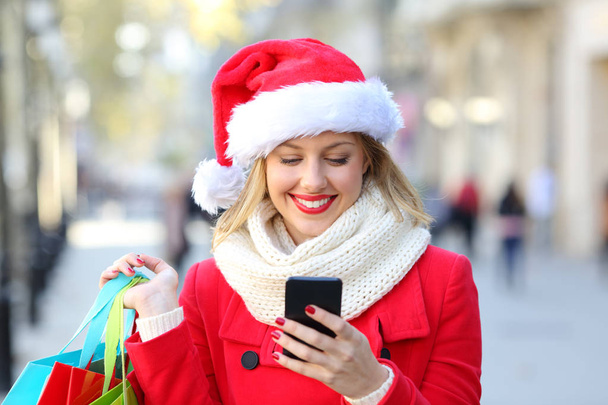 Happy shopper checking phone content on christmas in the street - 写真・画像