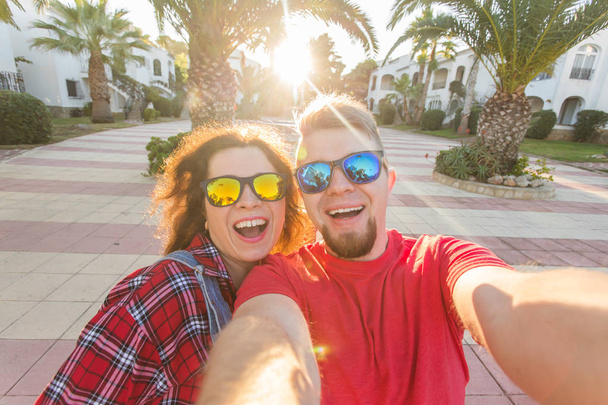 Путешествия, отдых и праздничная концепция - Забавная пара в солнечных очках, развлекающаяся и делающая селфи
 - Фото, изображение