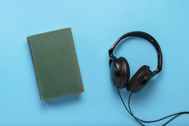 Réservez avec une couverture bleue et un casque noir sur un fond bleu. Concept de livres audio, auto-éducation. Couché plat, vue du dessus
. - Photo, image