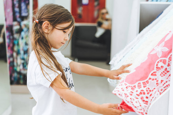 Menina em uma loja de tecidos escolhe um tecido multi-colorido
 - Foto, Imagem