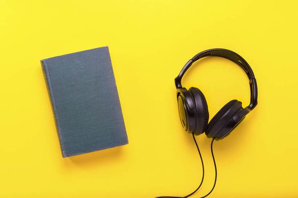 Book with a blue cover with text English and black headphones on a yellow background. Concept of audio books, self-education. Flat lay, top view. - Photo, Image