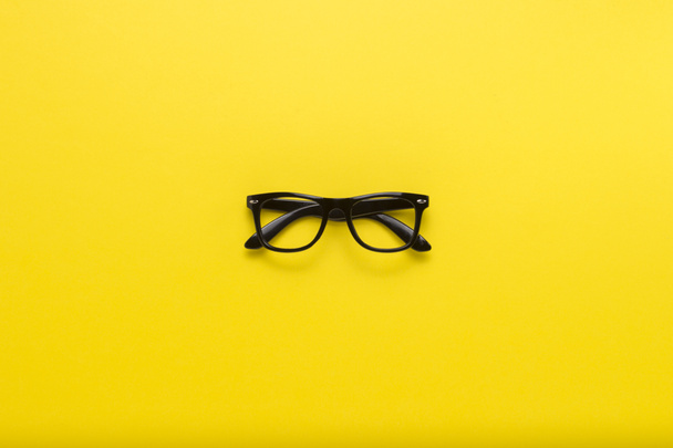 Black glasses on a yellow background. Flat lay, top view. - Photo, image