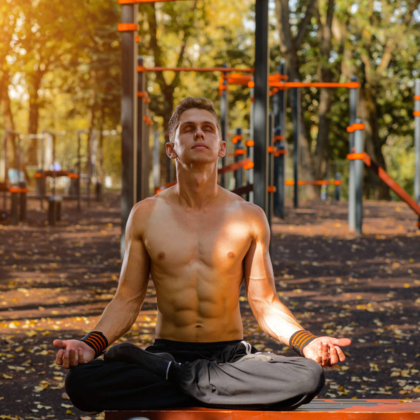 young male athlete on a street court sitting in a lotus yoga pose outdoors, practicing yoga, meditation exercises - Foto, Imagem