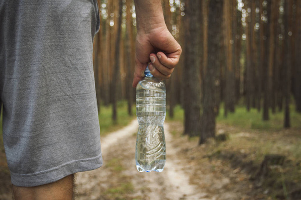 Man met een fles water op de achtergrond van een onverharde weg in het bos. Concept van de opleiding in de outdoor en wandelen in het bos en bergen. - Foto, afbeelding
