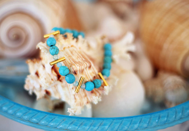 стильный браслет с бирюзовыми полудрагоценными камнями - размытый фон с раковинами
 - Фото, изображение