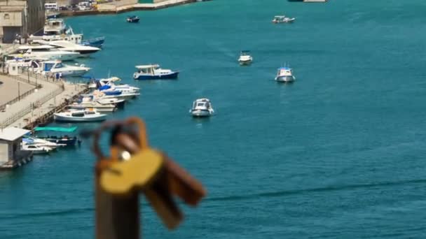 Padlocks against the backdrop of a blue bay, with motorized boats and the embankment. Focus moves slowly from one object to another. Blurred background of moving yachts by the sea. - Footage, Video