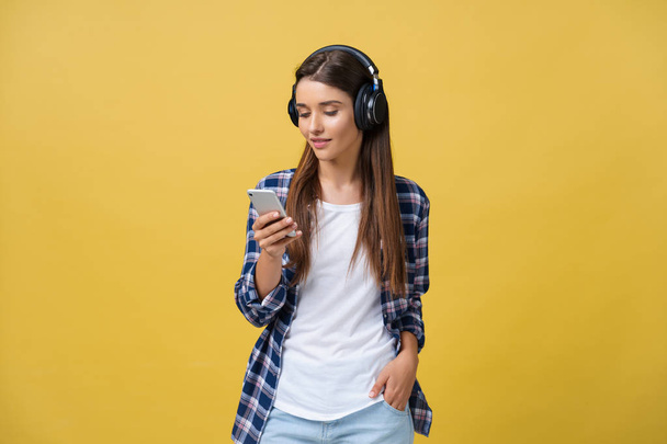 Beautiful young woman in headphones listening to music and singing on yellow background - Foto, afbeelding
