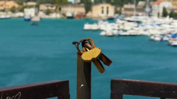 Padlocks against the backdrop of a blue bay, with motorized boats and the embankment. Blurred background of moving yachts by the sea. - Footage, Video