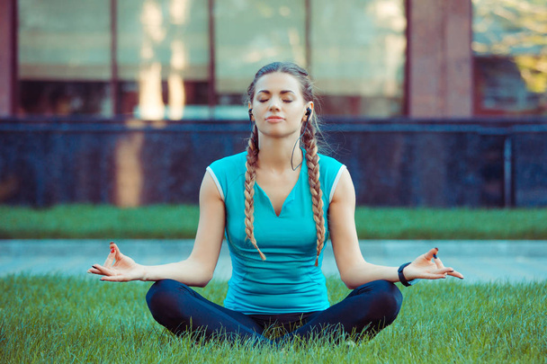 Молода спортсменка, сидячи на зеленому газоні в медитації, позує закритими очима
 - Фото, зображення