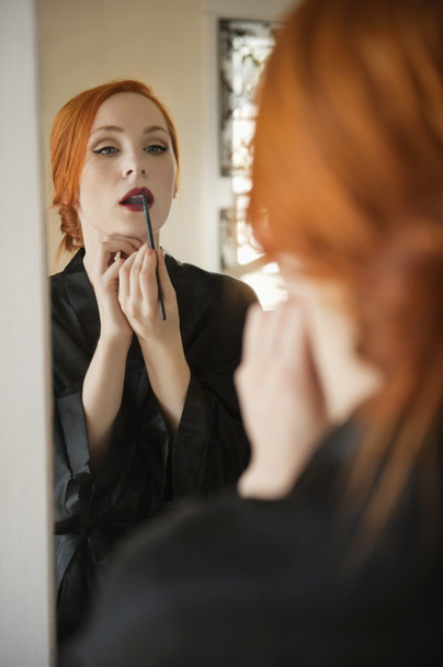 Young female applying lip liner in front of mirror - Foto, afbeelding