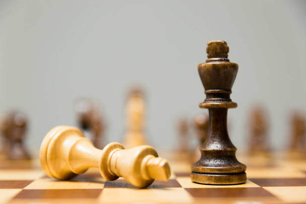 Due pezzi di scacchi re su una scacchiera con il re leggero sdraiato al suo fianco ai piedi del vittorioso re di legno scuro
 - Foto, immagini