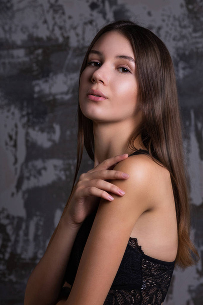 Test shoot of elegant brunette model with perfect skin posing in a black lace bra against grey wall - 写真・画像