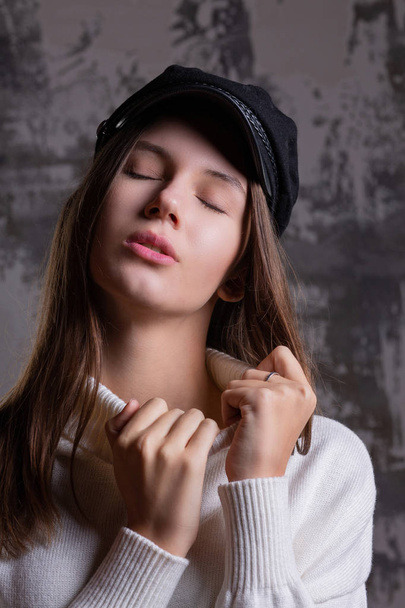Test shoot of tender brunette girl posing in stylish cap and knitted dress - 写真・画像