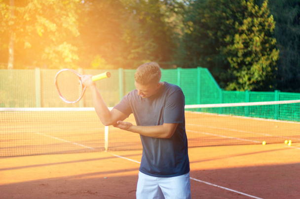 Handsome man on tennis court. Young tennis player. Pain in the elbow with sunlight in background - Photo, Image