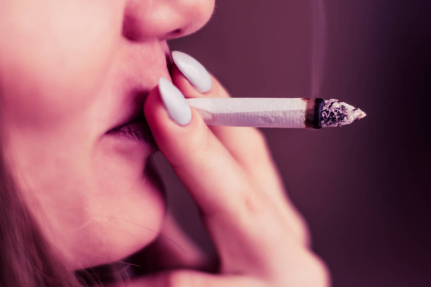 Joint in Frauenhand. eine Frau raucht Cannabiskraut, a. Rauch auf schwarzem Hintergrund. Konzepte des medizinischen Marihuanakonsums und der Legalisierung von Cannabis. auf schwarzem Hintergrund rosa Tönung - Foto, Bild