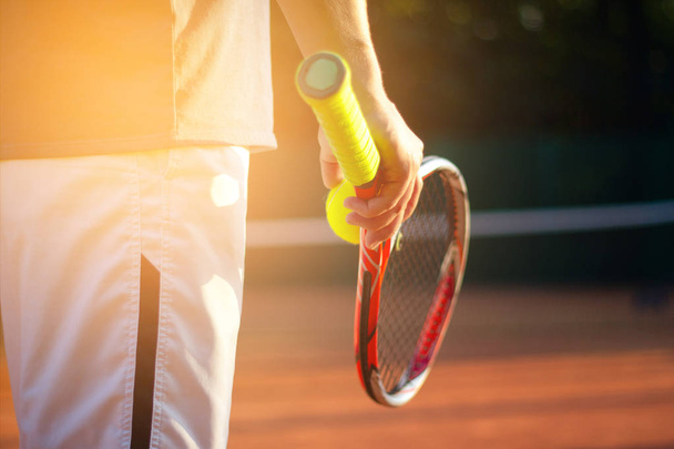 A tennis player prepares to serve a tennis ball during a match with sunlight in background - Φωτογραφία, εικόνα