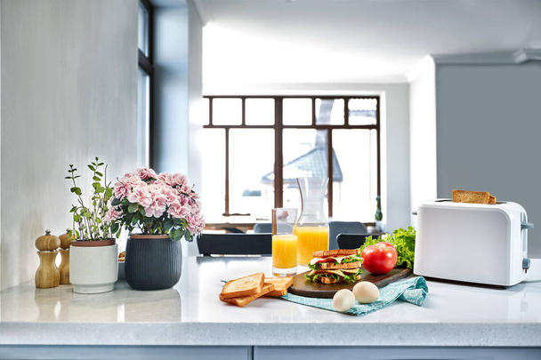 Белый электрический тостер с апельсиновым соком и сэндвичем на кухонном столе. Завтрак на уютной кухне
. - Фото, изображение