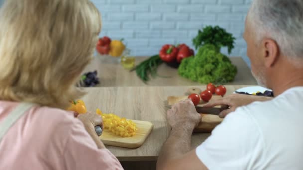 Elderly married couple cutting vegetables in kitchen, cooking dinner together - Video, Çekim