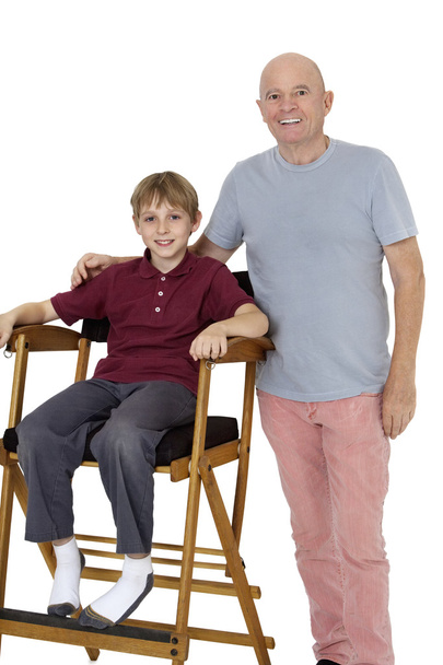 Portrait of senior man with pre-teen boy sitting on director's chair over white background - Фото, изображение