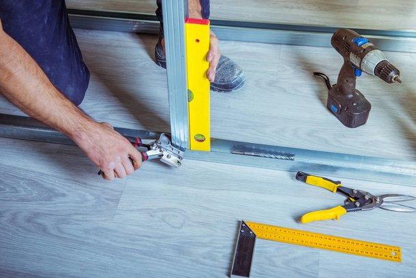 Drywall plaster stud crimpers in action. A person holding and using stud crimping tool in hand while building a metal drywall construction in a house during renovation - Fotoğraf, Görsel