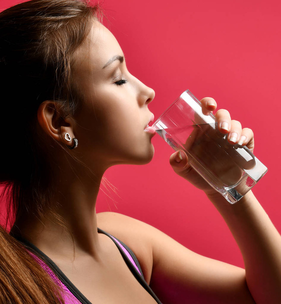 Sporty woman drinking water from highball glass on red background - Foto, Bild