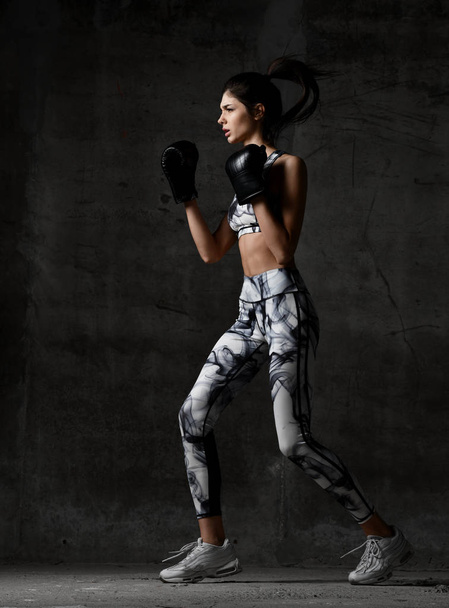 Young beautiful woman box trainer boxing in black gloves on concrete loft wall background - Fotografie, Obrázek