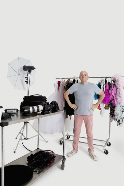 Portrait of senior man with hands on hips standing in front of clothes rack in studio - Fotó, kép