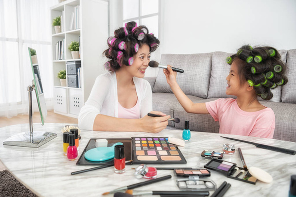 happy elegant lady feeling cheerful when her kid using brush helping her makeup with colorful cosmetic powder. - Foto, imagen