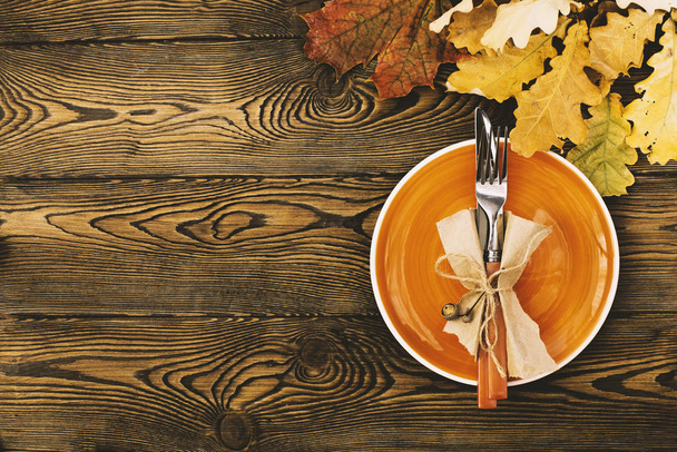 Nakrycie stołu jesienny w Święto Dziękczynienia. Pusta płyta, sztućce, barwne listowie, na drewnianym stole. Upadek jedzenie koncepcja - Zdjęcie, obraz