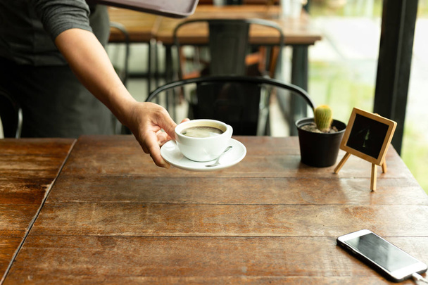 Garçom servindo xícara de café com telefone celular na mesa de café
 - Foto, Imagem