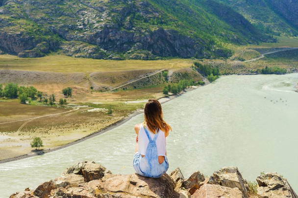 Девушка сидит на скалах в горах. Турист на вершине горы. Горная река. Летний день
 - Фото, изображение