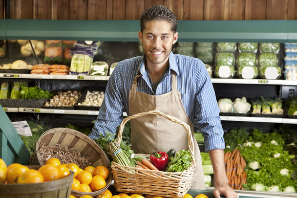 Portrait of a happy young salesman with vegetable basket in supermarket - Photo, image