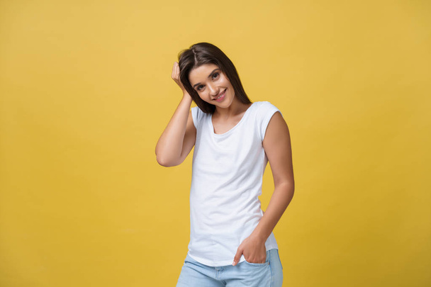 Lächelnd blickt die schöne junge Frau in weißem Hemd in die Kamera. dreiviertel Studioaufnahme auf gelbem Hintergrund. - Foto, Bild