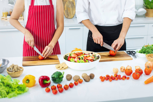 Mooie Aziatische vrouw in rode schort leren hoe om te koken en fruit salade in grote kom, meng onderwijs door Aziatische chef-kok in witte moderne keuken. - Foto, afbeelding