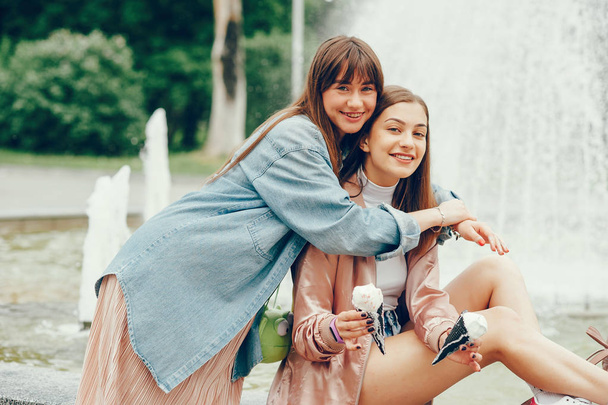 Two girls sitting near the fountain and going ice cream. - 写真・画像