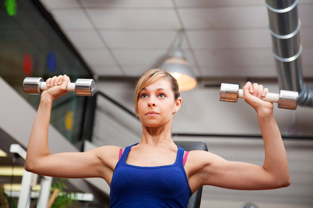 Portrait of young woman lifting dumbbells in fitness club - Photo, image